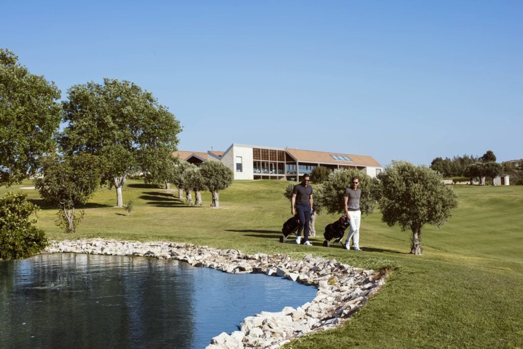 Golf-_-Clubhouse-1024x683jpg - Sovereign Estates Sovereign Estates Two men walking across a sunny golf course carrying golf bags toward a modern clubhouse in the distance 2026 Two men walking across a sunny golf course carrying golf bags toward a modern clubhouse in the distance