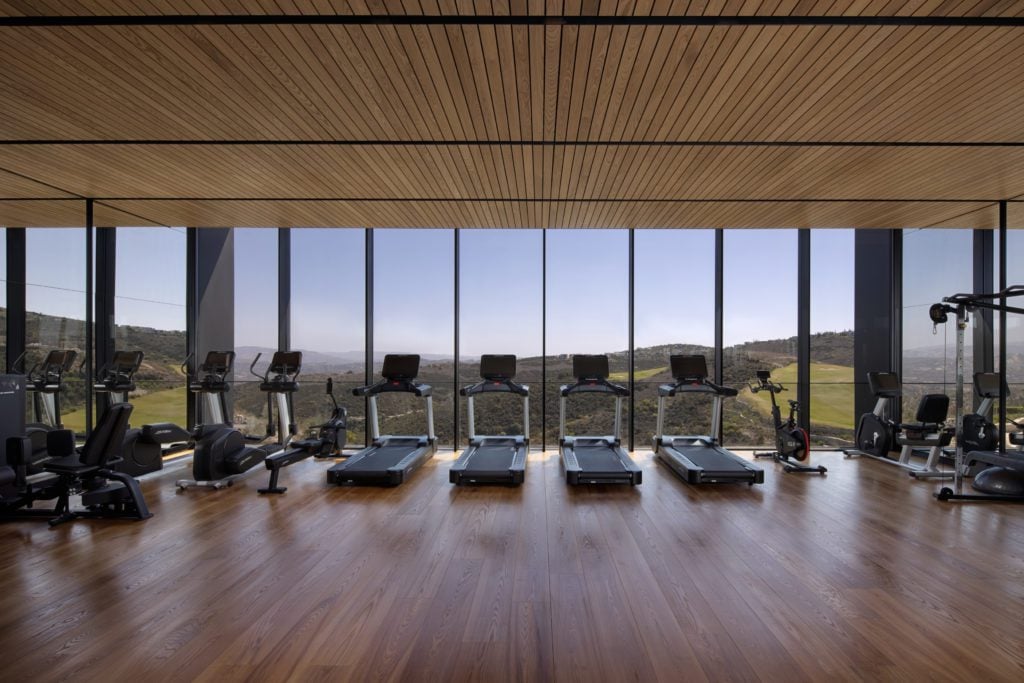 Minthis-Spa-Gym-1024x683jpg - Sovereign Estates Sovereign Estates Gym interior with a row of treadmills facing a large glass wall and scenic hills outside wooden floor and ceiling panels 2026 Gym interior with a row of treadmills facing a large glass wall and scenic hills outside wooden floor and ceiling panels