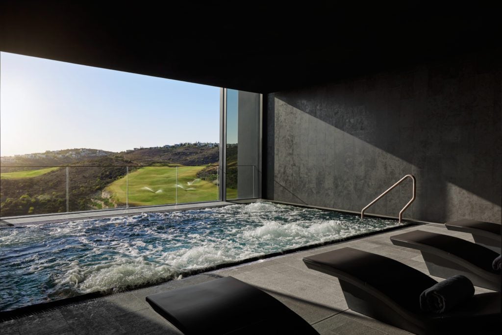 Minthis-Spa-Hydropool-1024x683jpg - Sovereign Estates Sovereign Estates Indoor pool area with a glass wall showing a sunny golf course and rolling hills outside and lounge chairs in the foreground 2026 Indoor pool area with a glass wall showing a sunny golf course and rolling hills outside and lounge chairs in the foreground