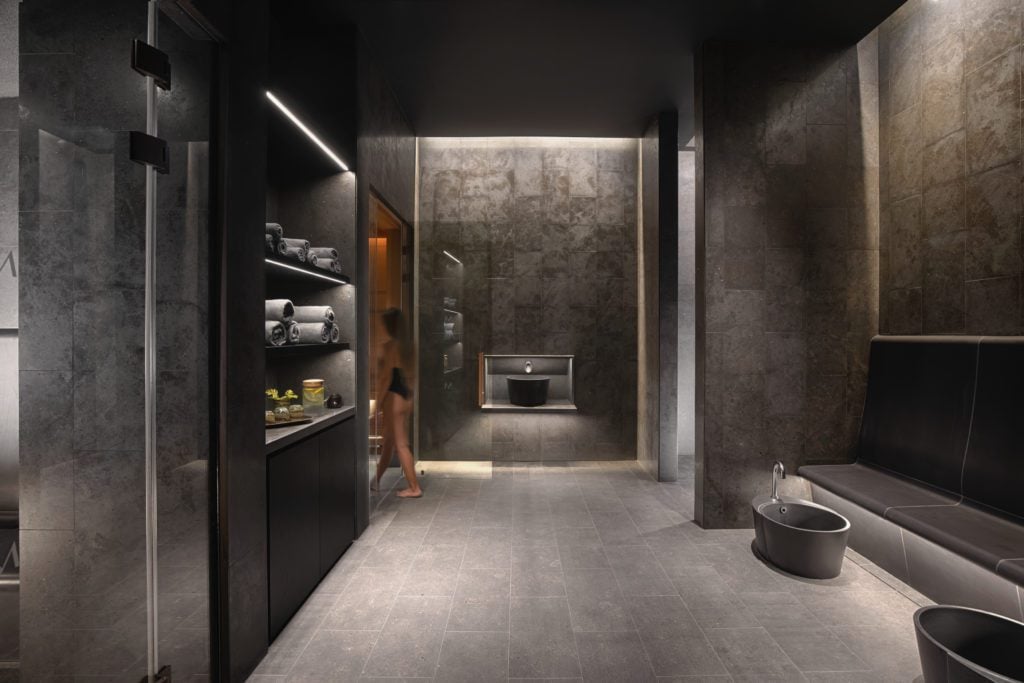 Minthis-Spa-Thermal-Suites--1024x683jpg - Sovereign Estates Sovereign Estates Luxurious dark spa locker room with towel shelves and a person walking toward the glass door 2026 Luxurious dark spa locker room with towel shelves and a person walking toward the glass door