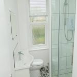 Sovereign Estates   Compact white bathroom with a glass enclosed shower a white sink and a toilet under a frosted window with blinds blue patterned floor tiles 2026 Compact white bathroom with a glass enclosed shower a white sink and a toilet under a frosted window with blinds blue patterned floor tiles
