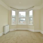 Sovereign Estates   Empty beige carpeted room with a white radiator on the left and a three panel bay window overlooking rooftops at dusk light informative 2026 Empty beige carpeted room with a white radiator on the left and a three panel bay window overlooking rooftops at dusk light informative