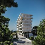 Sovereign Estates   White modern apartment building with horizontal balconies set in a landscaped area with trees and a driveway leading to the entrance blue sky and distant sea in the background 2026 White modern apartment building with horizontal balconies set in a landscaped area with trees and a driveway leading to the entrance blue sky and distant sea in the background