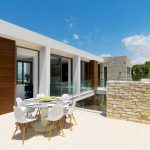 Sovereign Estates   Outdoor terrace with a round dining table and white chairs glass railing and stone walls under a bright blue sky 2026 Outdoor terrace with a round dining table and white chairs glass railing and stone walls under a bright blue sky