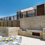 Sovereign Estates   Outdoor terrace with stone walls a built in barbecue and a round dining table set for six under bright sun 2026 Outdoor terrace with stone walls a built in barbecue and a round dining table set for six under bright sun