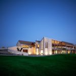 Sovereign Estates   Modern stone house at twilight with warm interior lights and a large green lawn in front 2026 Modern stone house at twilight with warm interior lights and a large green lawn in front