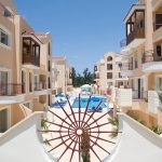 Sovereign Estates   Resort courtyard with beige buildings flanking a central blue pool seen from a white balustrade with a large circular metal wheel sculpture in the foreground on a sunny day 2026 Resort courtyard with beige buildings flanking a central blue pool seen from a white balustrade with a large circular metal wheel sculpture in the foreground on a sunny day