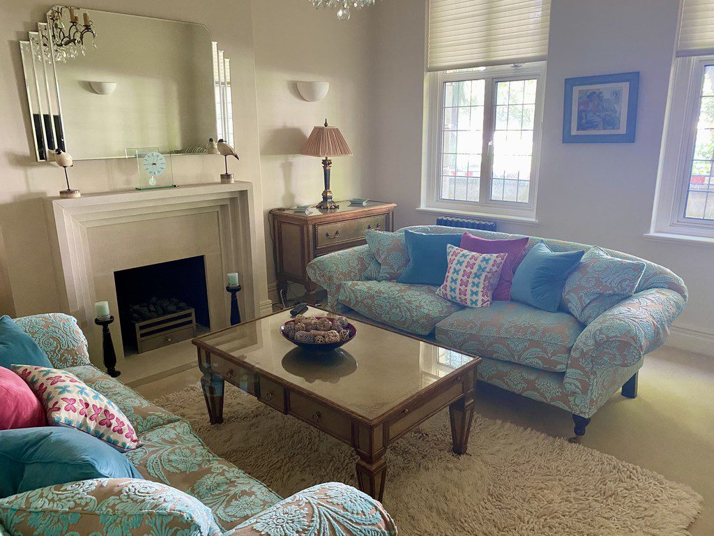 IMG_21_19_largejpg - Sovereign Estates Sovereign Estates Living room with two light blue patterned sofas colorful cushions a glass coffee table and a fireplace with a large mirror above 2026 Living room with two light blue patterned sofas colorful cushions a glass coffee table and a fireplace with a large mirror above