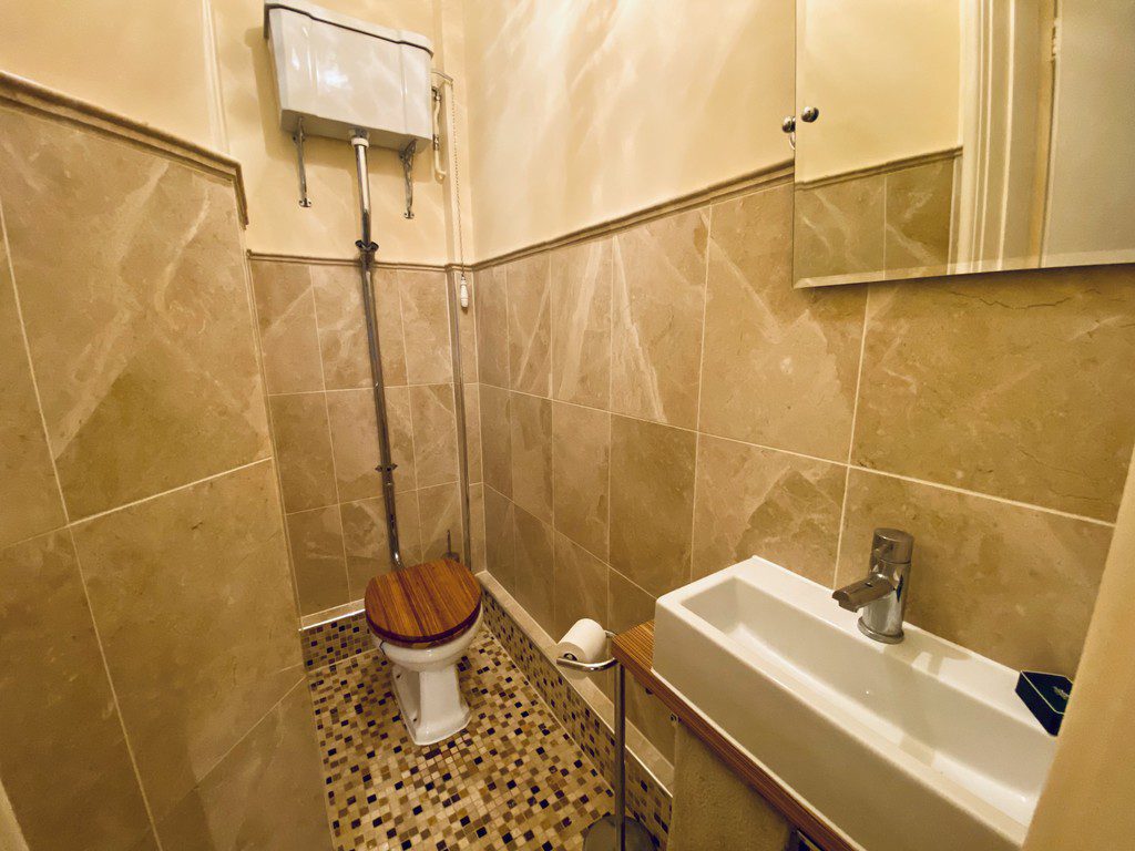 IMG_21_1_largejpg - Sovereign Estates Sovereign Estates Small beige tiled bathroom with a white toilet that has a wooden seat and a high mounted cistern with exposed pipes a white rectangular sink with a chrome faucet is adjacent and a wall cabinet mirror is visible above 2026 Small beige tiled bathroom with a white toilet that has a wooden seat and a high mounted cistern with exposed pipes a white rectangular sink with a chrome faucet is adjacent and a wall cabinet mirror is visible above