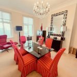 IMG_21_27_largejpg - Sovereign Estates Sovereign Estates Dining room with a glass dining table surrounded by six red striped chairs a crystal chandelier and a black sideboard with a square framed mirror above it 2026 Dining room with a glass dining table surrounded by six red striped chairs a crystal chandelier and a black sideboard with a square framed mirror above it