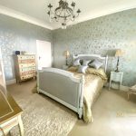Sovereign Estates   Elegant bedroom with a white ornate bed gold comforter and pale blue gold damask wallpaper matching nightstands and lamps flank the bed 2026 Elegant bedroom with a white ornate bed gold comforter and pale blue gold damask wallpaper matching nightstands and lamps flank the bed