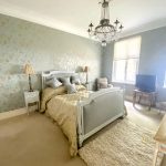 Sovereign Estates   Elegant master bedroom with a carved gray bed gold quilt and crystal chandelier overhead in soft blue floral walls 2026 Elegant master bedroom with a carved gray bed gold quilt and crystal chandelier overhead in soft blue floral walls