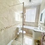 Sovereign Estates   Bright beige tiled bathroom with a bathtub under a window glass shower door and a white vanity with mirror on the right side 2026 Bright beige tiled bathroom with a bathtub under a window glass shower door and a white vanity with mirror on the right side