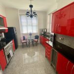 IMG_21_3_largejpg - Sovereign Estates Sovereign Estates Modern kitchen with glossy red cabinets black countertops and stainless steel appliances a small round dining table and two chairs sit by a window with blinds under a black chandelier 2026 Modern kitchen with glossy red cabinets black countertops and stainless steel appliances a small round dining table and two chairs sit by a window with blinds under a black chandelier