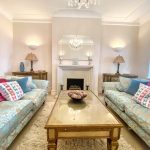 Sovereign Estates   Bright living room with two floral blue sofas facing a glass topped coffee table and a fireplace beneath a decorative mirror 2026 Bright living room with two floral blue sofas facing a glass topped coffee table and a fireplace beneath a decorative mirror