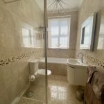 IMG_21_7_largejpg - Sovereign Estates Sovereign Estates Beige tiled bathroom with a glass shower enclosure toilet sink with a curved vanity and a tub beneath a window a brown towel hangs on a rack 2026 Beige tiled bathroom with a glass shower enclosure toilet sink with a curved vanity and a tub beneath a window a brown towel hangs on a rack