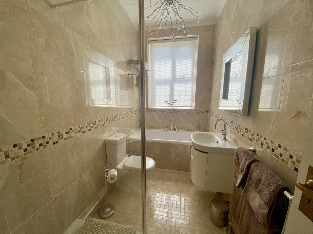 IMG_21_7_largejpg - Sovereign Estates Sovereign Estates Beige tiled bathroom with a glass shower enclosure toilet sink with a curved vanity and a tub beneath a window a brown towel hangs on a rack 2026 Beige tiled bathroom with a glass shower enclosure toilet sink with a curved vanity and a tub beneath a window a brown towel hangs on a rack