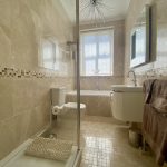IMG_21_8_largejpg - Sovereign Estates Sovereign Estates Modern beige tiled bathroom with a glass shower enclosure toilet and a white vanity under a window 2026 Modern beige tiled bathroom with a glass shower enclosure toilet and a white vanity under a window