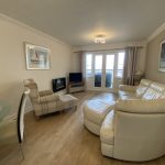 Sovereign Estates   Bright living room with a white leather sofa round ottoman and plaid armchair facing a TV near glass balcony doors 2026 Bright living room with a white leather sofa round ottoman and plaid armchair facing a TV near glass balcony doors
