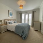 Sovereign Estates   Double bed with white textured cover and blue throw two matching bedside tables with lamps in a bright bedroom with French doors and curtains 2026 Double bed with white textured cover and blue throw two matching bedside tables with lamps in a bright bedroom with French doors and curtains