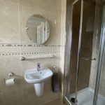Sovereign Estates   Bathroom with a pedestal sink round mirror towel bar and a glass enclosed shower in beige tiles 2026 Bathroom with a pedestal sink round mirror towel bar and a glass enclosed shower in beige tiles