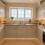 Sovereign Estates   Light gray kitchen with white shaker cabinets under cabinet lighting and a double sink beneath a window 2026 Light gray kitchen with white shaker cabinets under cabinet lighting and a double sink beneath a window
