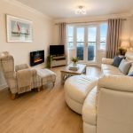 Sovereign Estates   Bright living room with a white leather sofa plaid armchair coffee table and balcony doors to outside light 2026 Bright living room with a white leather sofa plaid armchair coffee table and balcony doors to outside light