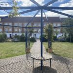 IMG_23_23_largejpg - Sovereign Estates Sovereign Estates Blue metal gazebo frame over a circular wooden table on a brick paved courtyard with benches and a grassy garden behind 2026 Blue metal gazebo frame over a circular wooden table on a brick paved courtyard with benches and a grassy garden behind