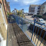 IMG_23_44_largejpg - Sovereign Estates Sovereign Estates View from a narrow wooden balcony with blue metal railing overlooking a sunny street with parked cars and apartment buildings 2026 View from a narrow wooden balcony with blue metal railing overlooking a sunny street with parked cars and apartment buildings
