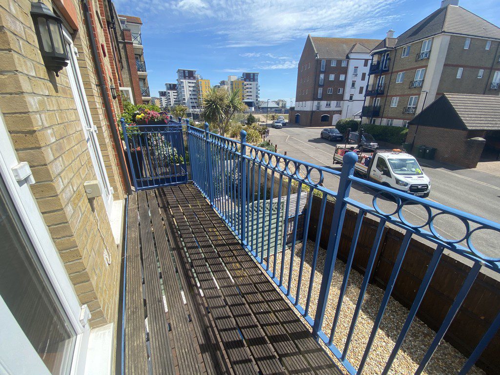 IMG_23_44_largejpg - Sovereign Estates Sovereign Estates View from a narrow wooden balcony with blue metal railing overlooking a sunny street with parked cars and apartment buildings 2026 View from a narrow wooden balcony with blue metal railing overlooking a sunny street with parked cars and apartment buildings