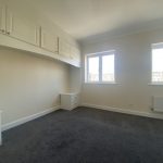 IMG_23_60_largejpg - Sovereign Estates Sovereign Estates Empty bedroom with white built in cabinets along the left wall dark carpet two windows showing a cityscape and a radiator under the right window 2026 Empty bedroom with white built in cabinets along the left wall dark carpet two windows showing a cityscape and a radiator under the right window
