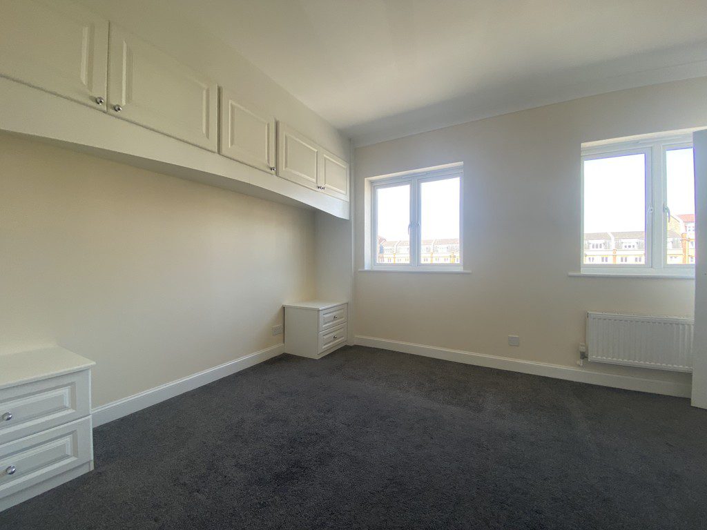 IMG_23_60_largejpg - Sovereign Estates Sovereign Estates Empty bedroom with white built in cabinets along the left wall dark carpet two windows showing a cityscape and a radiator under the right window 2026 Empty bedroom with white built in cabinets along the left wall dark carpet two windows showing a cityscape and a radiator under the right window