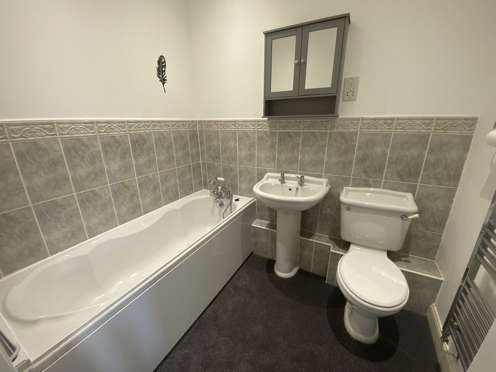 IMG_23_76_largejpg - Sovereign Estates Sovereign Estates Bathroom with white bathtub pedestal sink and toilet along tiled walls a gray wall cabinet above and a feather decal on the wall 2026 Bathroom with white bathtub pedestal sink and toilet along tiled walls a gray wall cabinet above and a feather decal on the wall