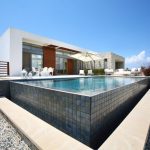 Sovereign Estates   Modern white villa with a rectangular tiled infinity pool and lounge area under a sun umbrella on a gravel landscape 2026 Modern white villa with a rectangular tiled infinity pool and lounge area under a sun umbrella on a gravel landscape