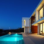 Sovereign Estates   Modern two story house with large glass windows stone and wood accents and an illuminated poolside patio at dusk 2026 Modern two story house with large glass windows stone and wood accents and an illuminated poolside patio at dusk