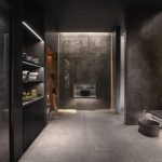 Sovereign Estates   Modern spa locker room with dark stone walls towel shelves on the left a person walking toward a glass door and a sink at the far wall 2026 Modern spa locker room with dark stone walls towel shelves on the left a person walking toward a glass door and a sink at the far wall