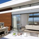 Sovereign Estates   Modern outdoor patio with a stone counter food spread and glass doors opening into a living room overlooking a city view 2026 Modern outdoor patio with a stone counter food spread and glass doors opening into a living room overlooking a city view
