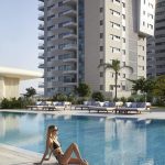 Sovereign Estates   Woman in a black bikini sits at the edge of a swimming pool with modern apartment buildings in the background 2026 Woman in a black bikini sits at the edge of a swimming pool with modern apartment buildings in the background
