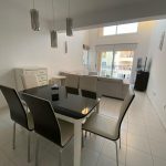 Sovereign Estates   Open plan dining and living area with a glass top table and six white chairs white cabinets and a balcony view from large windows 2026 Open plan dining and living area with a glass top table and six white chairs white cabinets and a balcony view from large windows