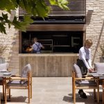 Sovereign Estates   Outdoor restaurant patio with a chef grilling behind an open kitchen while a server arranges tables in the foreground 2026 Outdoor restaurant patio with a chef grilling behind an open kitchen while a server arranges tables in the foreground