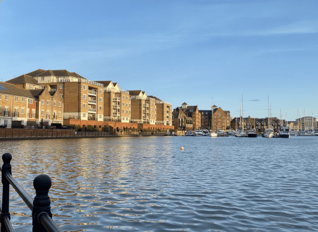 e334eaf3fc444763badc629eb2409fe2 - Sovereign Estates Sovereign Estates Harbor scene with boats docked along a brick riverside promenade and row of brick buildings beside calm water 2026 Harbor scene with boats docked along a brick riverside promenade and row of brick buildings beside calm water