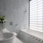 Sovereign Estates   Luxurious marble bathroom with a rectangular bathtub by a large window with striped blinds and two sinks with a vase of white lilies on the counter 2026 Luxurious marble bathroom with a rectangular bathtub by a large window with striped blinds and two sinks with a vase of white lilies on the counter