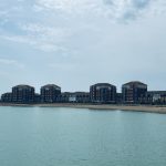 Sovereign Estates   Row of modern apartment buildings along a sandy coastal shore with calm water in the foreground and blue sky above 2026 Row of modern apartment buildings along a sandy coastal shore with calm water in the foreground and blue sky above