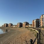 Sovereign Estates   Row of modern red brick apartment buildings along a paved seaside promenade with a calm bay on the left under a clear blue sky 2026 Row of modern red brick apartment buildings along a paved seaside promenade with a calm bay on the left under a clear blue sky