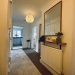 Sovereign Estates   Bright hallway with a rug runner radiator and a wall mounted shelf holding books and a potted plant in front of a large mirror 2026 Bright hallway with a rug runner radiator and a wall mounted shelf holding books and a potted plant in front of a large mirror