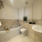 Sovereign Estates   Modern bathroom with white bathtub toilet and sink beige tiled walls and a striped rug on the floor 2026 Modern bathroom with white bathtub toilet and sink beige tiled walls and a striped rug on the floor