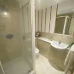 Sovereign Estates   Compact bathroom with a glass enclosed shower on the left beige tiled walls and a curved white sink under a large mirror 2026 Compact bathroom with a glass enclosed shower on the left beige tiled walls and a curved white sink under a large mirror