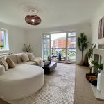 Sovereign Estates   Bright living room with a curved white sectional sofa beige cushions and a dark wood coffee table on a textured rug balcony doors and a fireplace with plants nearby 2026 Bright living room with a curved white sectional sofa beige cushions and a dark wood coffee table on a textured rug balcony doors and a fireplace with plants nearby