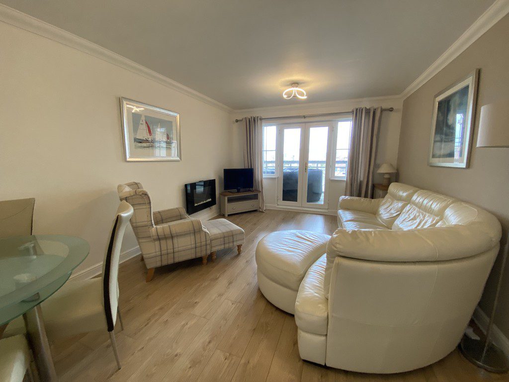 IMG_25_25_largejpg - Sovereign Estates Sovereign Estates Bright living room with white leather curved sofa and ottoman a plaid armchair a TV on a stand and an electric fireplace 2026 Bright living room with white leather curved sofa and ottoman a plaid armchair a TV on a stand and an electric fireplace