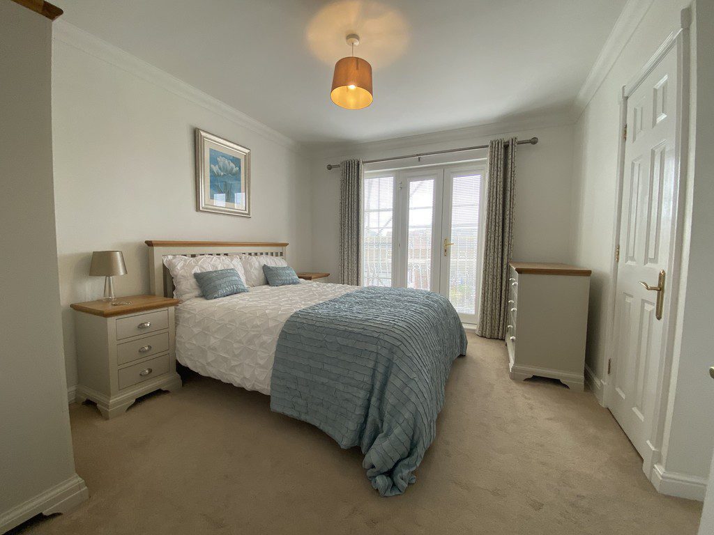 IMG_25_29_largejpg - Sovereign Estates Sovereign Estates Cozy bedroom with a white quilt bed blue throw and pillows twin nightstands with lamps and French doors to the outdoors 2026 Cozy bedroom with a white quilt bed blue throw and pillows twin nightstands with lamps and French doors to the outdoors